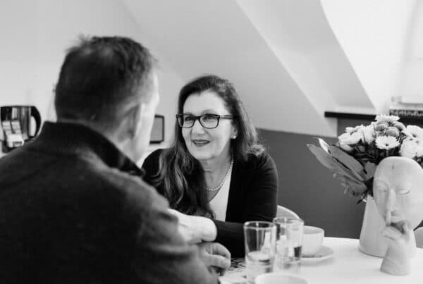 Ein Paar sitzt sich am Tisch gegenüber. Sie nimmt seine Hand. Symbol für Hoffnung und Neuanfang aus der Situation als das Paar in der Krise steckt